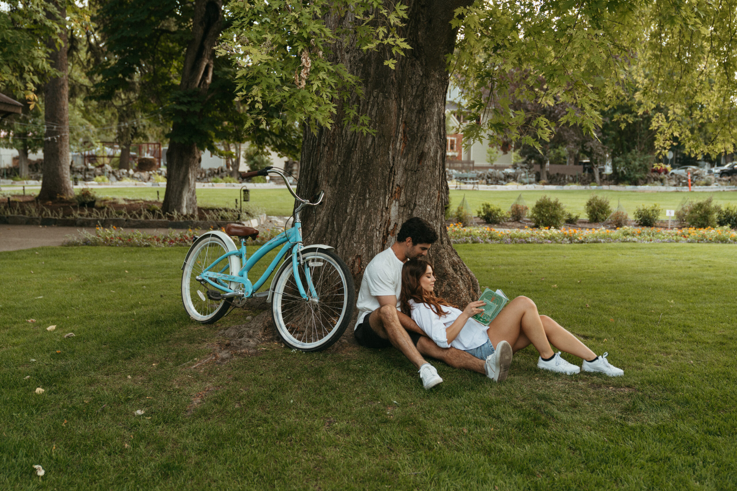 a couple sitting underneath a tree with a bike next to them